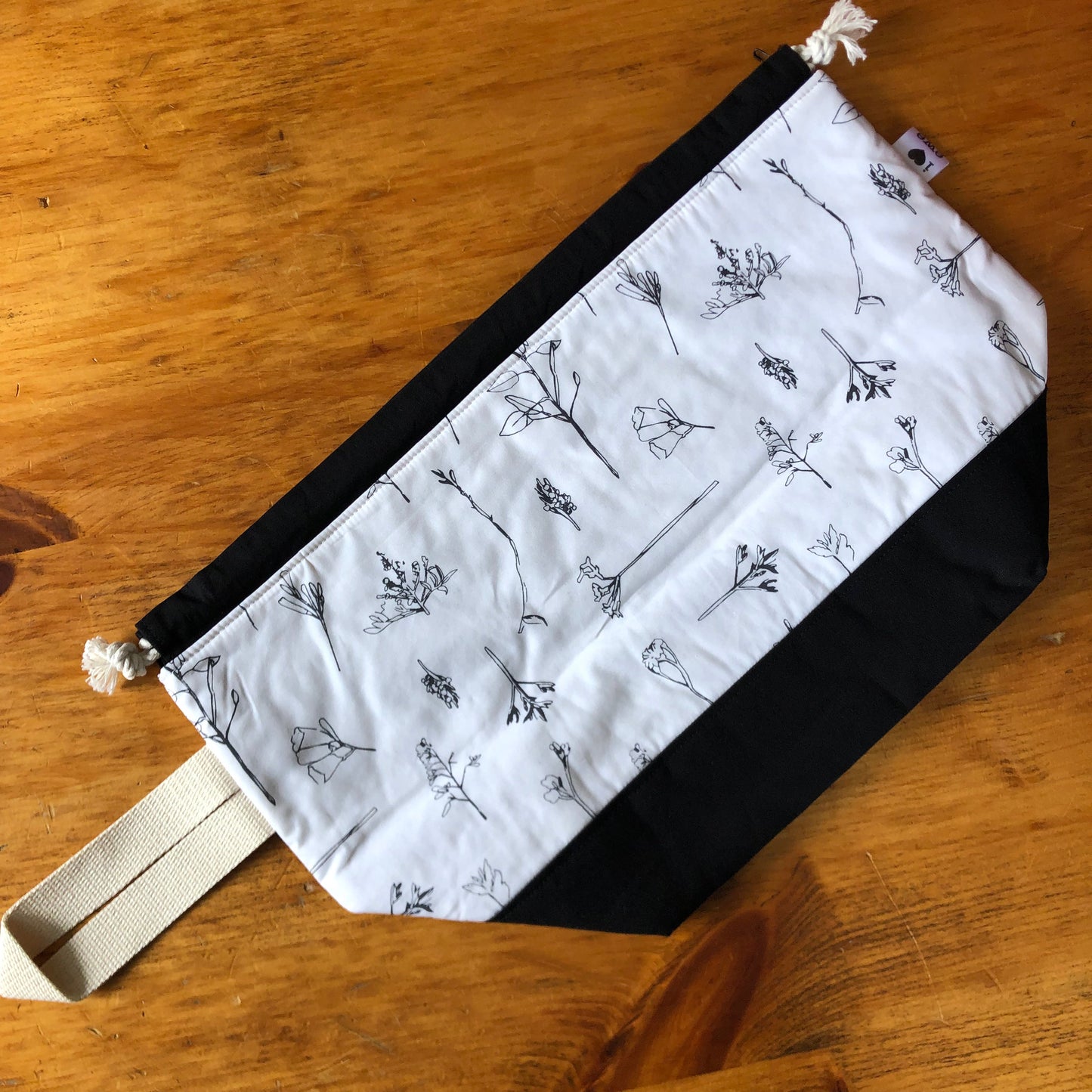 Ivory coloured drawstring bag with black bottom and black flowering grasses or wildflowers