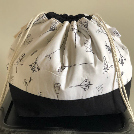 Ivory coloured drawstring bag with black bottom and black flowering grasses or wildflowers