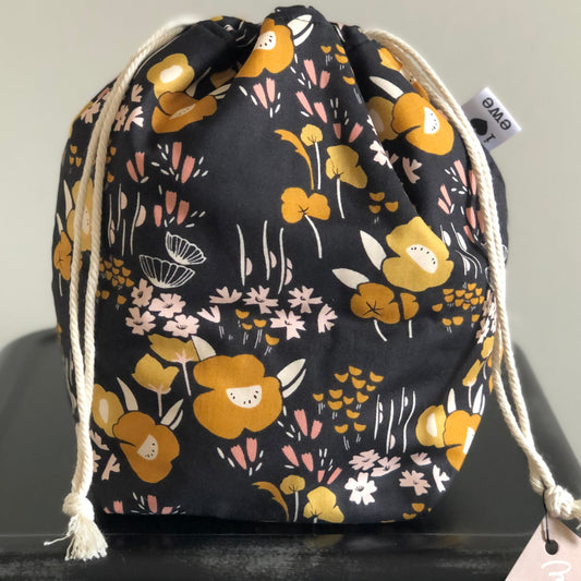 Black bag with cotton drawstring and a flowering print in mustards and pinks.